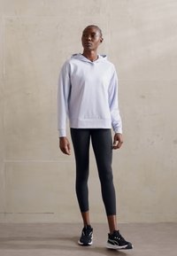 Világos levendula színű kapucnis pulóver hosszú ujjakkal és laza szabással, fekete leggings-szel és fekete sportcipőkkel párosítva.