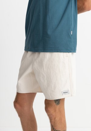 Teal cotton t-shirt with short sleeves paired with cream-colored shorts featuring a label on the hem, showing a relaxed fit and casual design.