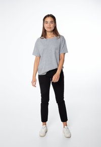 Camiseta gris de manga corta con un bolsillo en el pecho, combinada con jeans skinny negros y zapatillas blancas, con un fondo blanco liso.