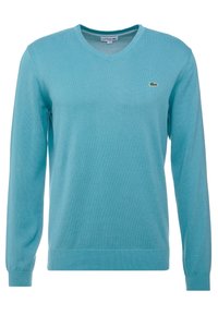 Ljusblå långärmad V-ringad tröja med ribbade manschetter och nederkant, med en liten grön Lacoste krokodil-logotyp på vänster bröst.