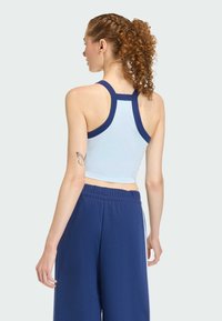 Svijetloplava sportska majica skraćenog kroja s tamnoplavim trakama. Tkanina izgleda glatko, a dizajn ima stil trkača.