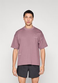 Χαλαρή, κοντομάνικη μπλούζα σε χρώμα σκουριασμένο ροζ με το κείμενο «τρέξε με τη νύχτα» σε λευκό, με λαιμόκοψη crew και διακριτική σήμανση.