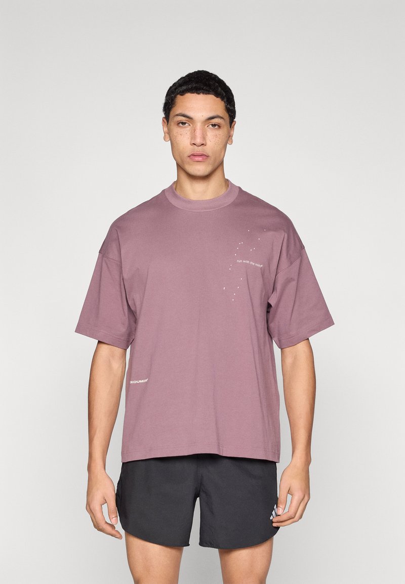 Χαλαρή, κοντομάνικη μπλούζα σε χρώμα σκουριασμένο ροζ με το κείμενο «τρέξε με τη νύχτα» σε λευκό, με λαιμόκοψη crew και διακριτική σήμανση.