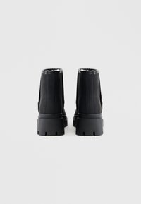 Melnas potītes zābaki ar gludu ādas apdari, mīkstu oderi un biezām gumijas zolēm ar izgriezuma rakstiem. Pielāgota pieguļošā forma ar teksturētiem akcentiem.