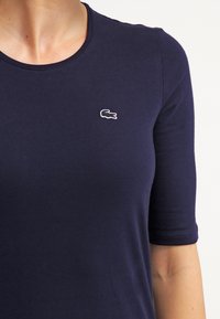 Mörkblå bomulls-t-shirt med rund hals och korta ärmar, prydd med en vit broderad logotyp på bröstet. Mjuk textur, figursydd design.