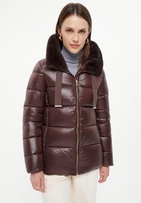 Brązowa kurtka puchowa z kołnierzem z futerka sztucznego, z zapięciem na zamek błyskawiczny, pikowanym fasonem i kontrastującymi paskami materiału. Gładka tekstura i błyszczące wykończenie.