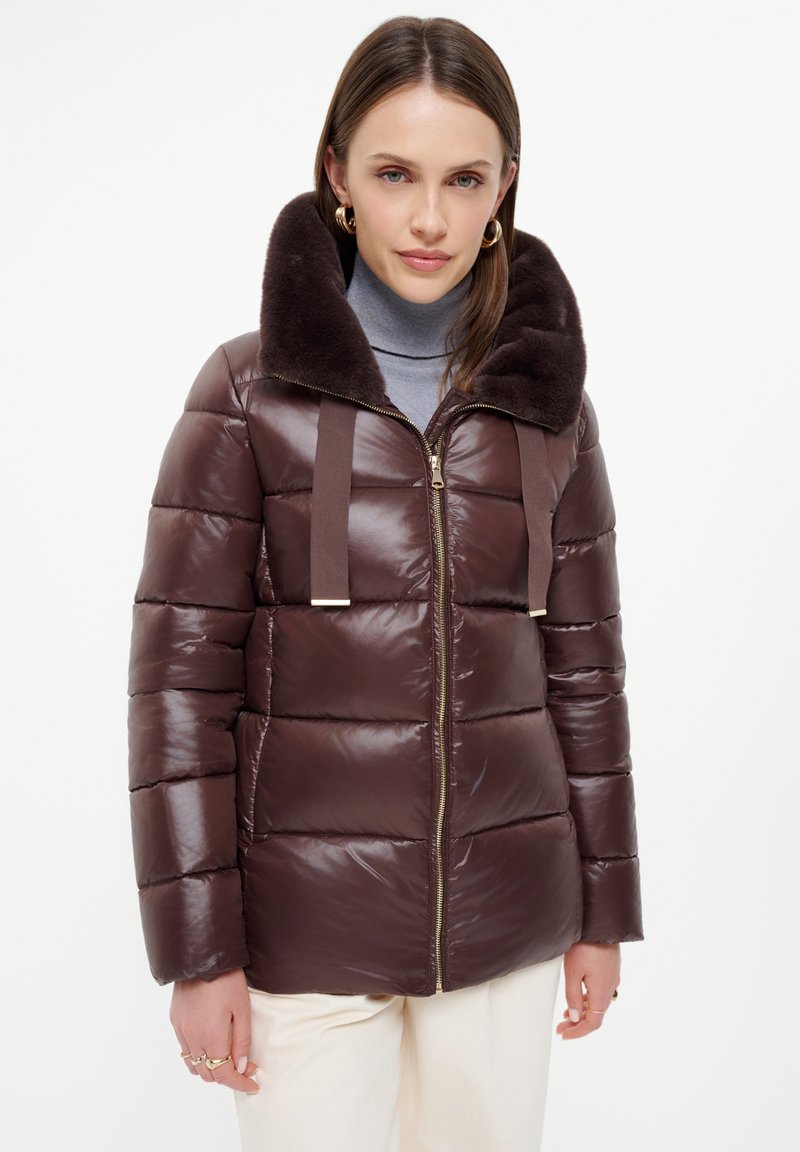 Brązowa kurtka puchowa z kołnierzem z futerka sztucznego, z zapięciem na zamek błyskawiczny, pikowanym fasonem i kontrastującymi paskami materiału. Gładka tekstura i błyszczące wykończenie.