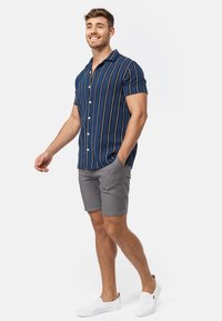 Blå kortærmet skjorte med hvide striber, knaplukning foran, parret med grå shorts og hvide slip-on sko. Afslappet pasform, letvægtsstof.
