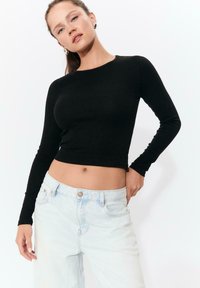 Schwarzes langärmliges Crop-Top aus weichem Stoff mit Rundhalsausschnitt, kombiniert mit hellblauen hochgeschnittenen Jeans mit Knopfverschluss.