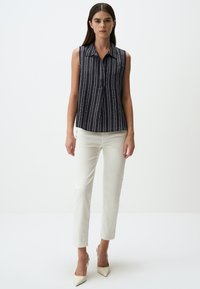 Blusa senza maniche blu navy con righe bianche verticali, frontale con bottoni e colletto classico; abbinata a pantaloni bianchi aderenti e tacchi a punta.