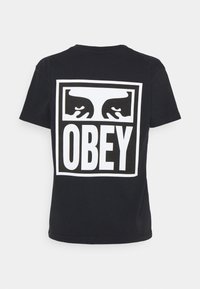 Černé bavlněné tričko s velkou bílou grafikou se dvěma očima a slovem "OBEY" tučně uprostřed na zádech.