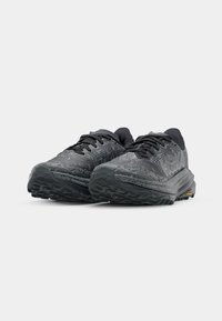 Black running shoes feature a textured upper, rounded toe, and a thick, patterned sole with distinct tread for grip.