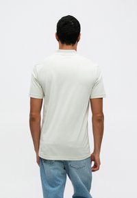 Jasnoszara, krótka koszulka polo z bawełny, z klasycznym kołnierzykiem i prostym wzorem, noszona z niebieskimi dżinsami.