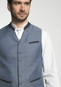 Blauer gemusterter Weste mit einer strukturierten Oberfläche, silbernen Knöpfen, schwarzer Einfassung am Ausschnitt und einer kleinen schwarzen Tasche auf der linken Seite.