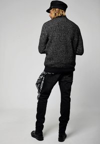 Pull noir et gris texturé avec un col rond, associé à un jean noir et un bandana décoratif noir et blanc noué à la taille.