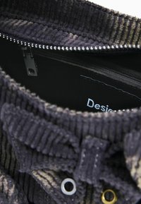 Interno di una borsa in velluto a coste nero con chiusura a zip, caratterizzato da una superficie testurizzata, dettagli in metallo dorato e argentato e un'etichetta visibile all'interno.