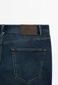 Tummansiniset farkut, joissa on nahkainen merkkipaikka takakammen ylhäällä. Ominaisuuksiin kuuluu yksi takatasku, jossa on erottuvaompeleet.