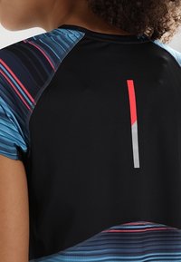 Top atlético negro con mangas estampadas en azul; cuenta con un acento vertical rojo y gris en la parte posterior; tejido suave y transpirable.