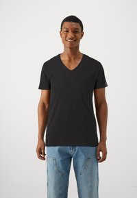 T-shirt negru cu decolteu în V, confecționat dintr-un material moale, cu mâneci scurte și croială lejeră, asortat cu blugi din denim de un albastru deschis, având detalii unice de cusutură.