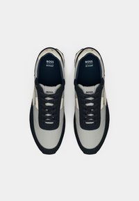 Pelni pelēkā un tumši zila krāsā, ar zemu dizainu, teksturētu auduma augšdaļu, tumšiem šņorēm un gumijas zoli ar kontrastējošiem akcentiem.