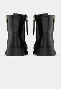 Paire de bottines noires en cuir avec fermeture éclair au dos et tirettes dorées, vues de dos sur fond blanc.