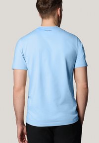 Jasnoniebieska bawełniana koszulka z krótkim rękawem i okrągłym dekoltem, z małym, drukowanym logo z tyłu, w pobliżu dekoltu.