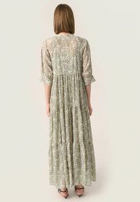 Largo vestido maxi en verde pálido con una tela texturizada y estampada. Cuenta con mangas de tres cuartos y una falda en capas y fluida.