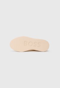 Sohle eines Schuhs in hellem Beige mit strukturierter Oberfläche. Das Wort "BOSS" ist auf der Sohle eingeprägt.