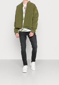 Oliivinvihreä pommitakki, vetoketjukiinnitys, ribbireunat. Valkoinen kukkapaidan alla, mustat slim fit -farkut ja valkoiset tennarit.