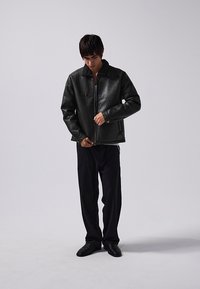 Black leather jacket with a textured finish, featuring a zip closure and a stand collar, paired with black loose-fitting trousers and shoes.