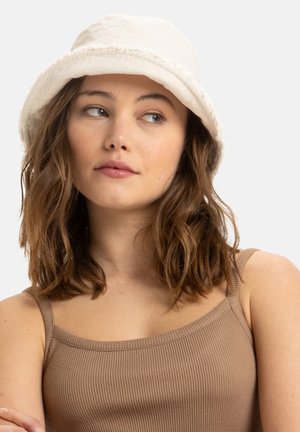 Chapeau seau de couleur crème en tissu doux, avec un large bord et une doublure intérieure texturée. Son design simple renforce sa polyvalence.