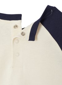 Crewet-farbenes kurzärmeliges Shirt mit marineblauen Raglanärmeln, ausgestattet mit drei Drucknöpfen am Ausschnitt und einer glatten Textur.