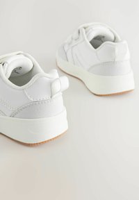 Baskets blanches avec une tige synthétique lisse et des accents texturés, de forme arrondie, et une semelle en caoutchouc avec un motif de bande de roulement beige.