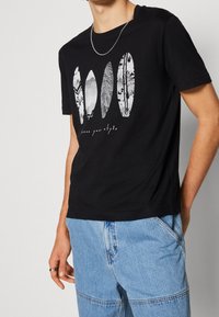 Czarny bawełniany t-shirt z grafiką przedstawiającą pięć stylizowanych desek surfingowych w odcieniach szarości i bieli, z okrągłym dekoltem i krótkimi rękawami.