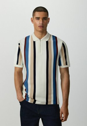 Young man with short hair wearing a short-sleeve polo shirt with vertical beige, blue, black, and maroon stripes and dark pants.