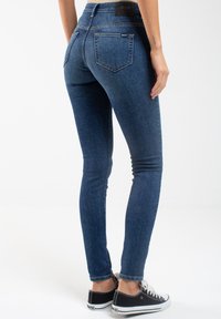 Tmavě modré skinny džíny s vysokým pasem, zadními kapsami a jemným vyblednutím. Kombinované s černými teniskami a bílými tkaničkami.