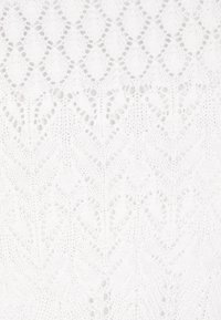 Fehér kötött textil, amelynek díszítő mintája összekapcsolódó gyémántok és levélformák, nyitott mintázattal és textúrázott részletezéssel.
