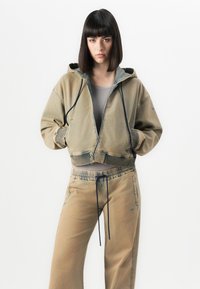 Cropped hooded jacket in khaki denim with contrasting inner lining, paired with matching drawstring trousers, featuring a relaxed fit.