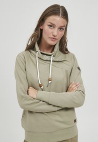 Felpa khaki con colletto alto, lacci e una fodera decorativa a motivo. Presenta una tasca laterale e dettagli in legno.