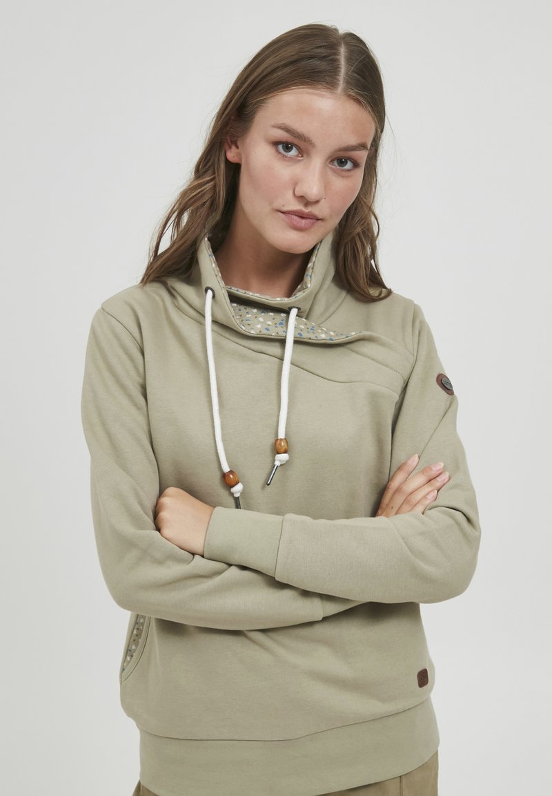 Felpa khaki con colletto alto, lacci e una fodera decorativa a motivo. Presenta una tasca laterale e dettagli in legno.