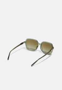 Ochelari de soare octogonali cu nuanțe verzi, lentile degradate maro și tempii metalici eleganți, având accente aurii pe balamale.