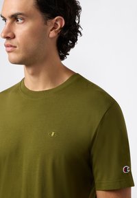Olivengroene t-shirt met korte mouwen van zacht materiaal, met een klein geborduurd logo op de borst en een kleurcontrasterende accent op de mouw.