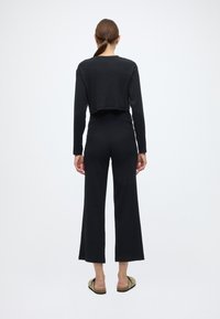 Conjunto preto canelado de duas peças composto por um top cropped de manga comprida e calças de perna larga com um ajuste confortável e textura suave.