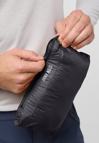 Schwarze Nylon-Aufbewahrungstasche mit einem Reißverschluss und "STOW AWAY" in Weiß bedruckt. Eine Hand greift den Reißverschluss-Zipper.