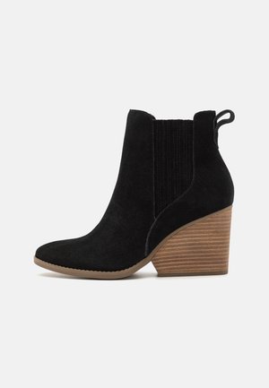 Black suede ankle boot with a pointed toe, ribbed elastic side, and a stacked wooden heel. Features a pull tab for easy wear.