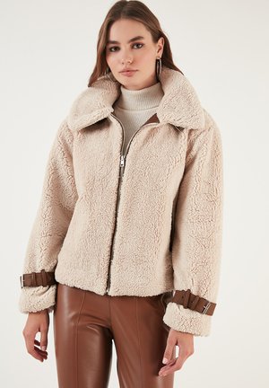 Kreemjas faux shearling jakk lai krae, lukuga ja pruuni nahast aktsentidega mansettides. Tekstuurne, mugav ja lühike disain.
