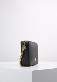 Černá kožená kabelka s texturovaným povrchem, zlatým  řetízkovým popruhem a zapínáním na zip. Kompaktní obdélníkový tvar s diskrétním logem.