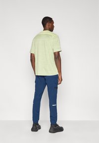 Ανοιχτό πράσινο κοντομάνικο πουκάμισο με υφή, σε συνδυασμό με σκούρο μπλε παντελόνι jogger με πλαϊνές τσέπες και ανακλαστικές λεπτομέρειες.