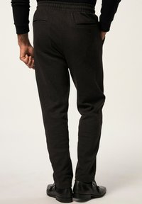 Pantalones oscuros de patrón espiga con cintura elástica, ajuste tapered y dos bolsillos traseros, combinados con zapatos negros.
