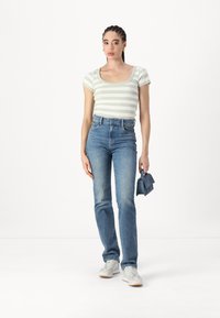 Λευκή και πράσινη ριγέ εφαρμοστή μπλούζα, ψηλόμεσα μπλε τζιν, ανοιχτόχρωμα αθλητικά παπούτσια και μικρή μπλε τσάντα. Απλός σχεδιασμός με χαλαρή εμφάνιση.